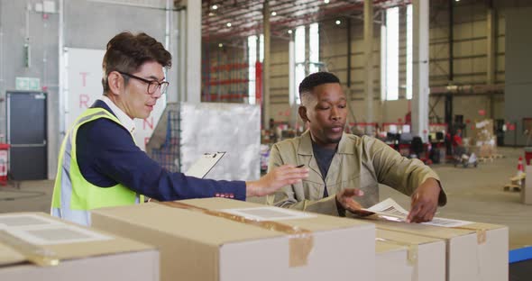 Diverse male workers with clipboard and boxes talking in warehouse