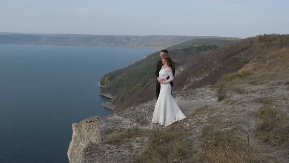 Newly Married Wedding Couple Stand Near a Cliff Overlooking the Sea