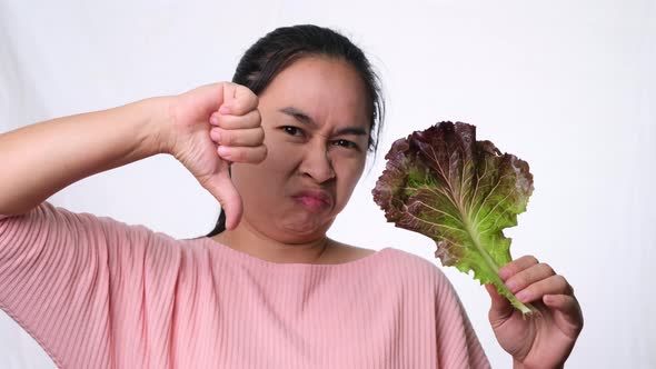 Asian woman hates fresh salad on white background in studio.