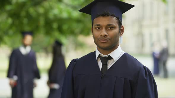 Guy in Graduation Outfit Crossing Arms with Diploma in Hand, Smiling Achievement