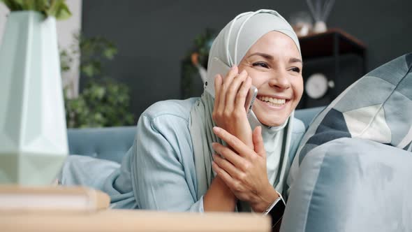 Happy Muslim Girl Wearing Traditional Hijab Talking on Mobile Phone Smiling Relaxing on Couch at