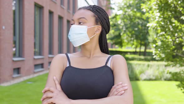 A Young Black Woman in a Face Mask Looks Around As She Waits for Someone - an Office Building