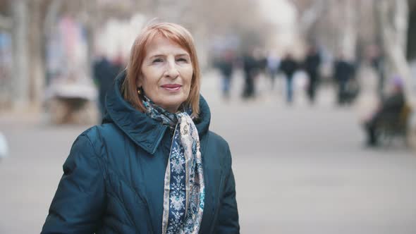 Smiling Senior Lady in Stylish Scarf Standing in Sunny Alley in Autumn in Slo-mo   