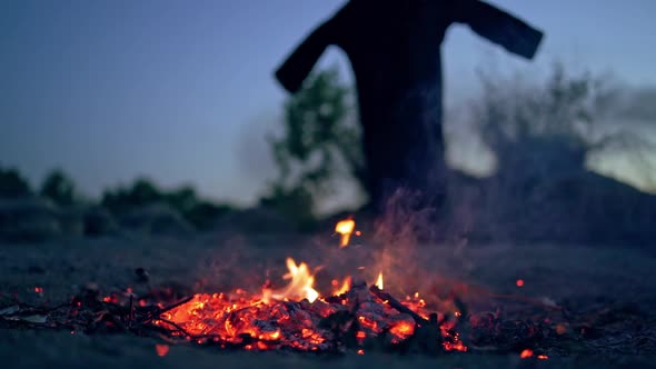 Embers of fire and scary witch outdoors. Death in black costume goes away from fire. Halloween conce