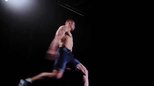 Young Pumped Man Doing a Flip in the Dark  Bright Lighting on the Background