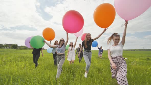 Girls Friends are Walking Across the Field with Large Balloons and Colorful Balloons