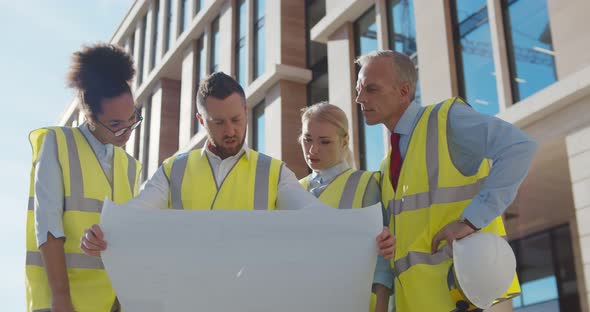 Team of Industrial Engineers Holding Blueprint Brainstorming About Project at Workplace