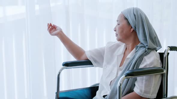 elderly woman with cancer sitting in a wheelchair looking out of the window while being hospitalized