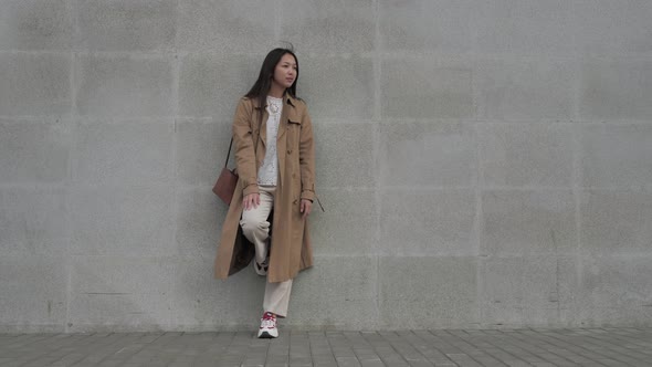 A Girl Fashionably Dressed Stands Leaning Her Foot Against a Concrete Wall 