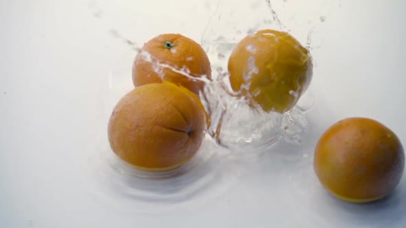 SLOMO of Oranges Falling into Water on White Backdrop