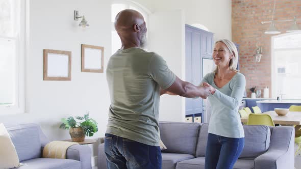 Mixed race senior couple dancing together in the living room at home