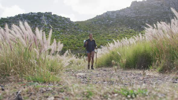 African american woman with trekking poles walking while trekking in the mountains