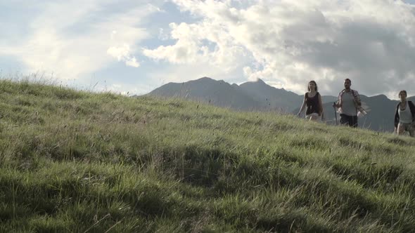 Young Friends Hiking Toward Camera on a Road in Mountain Outdoor Nature Scenery During Summer Day