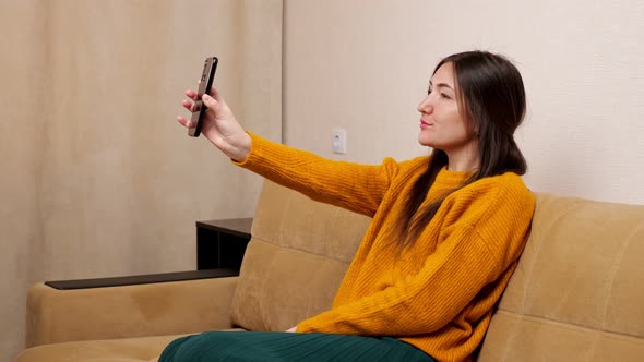 Young Brunette Holds Smartphone and Poses Into Front Camera