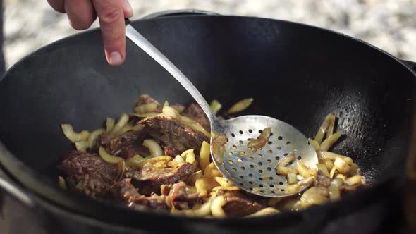 Stirring Meat and Onions Stewing in a Cauldron with a Slotted Spoon