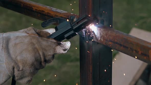 Closeup Worker Hand with Welding Machine Fixes Fence