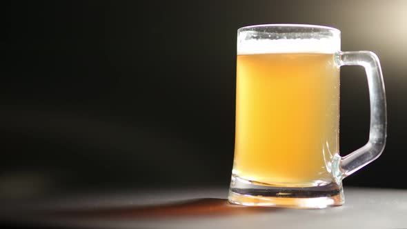 Big Mug of Cold Light Gold Fresh Beer Rotating Isolated at Black Lighting Background