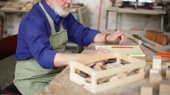 Concept of Diy. Old Man Is Making a Sketch of Birds House From Wood.