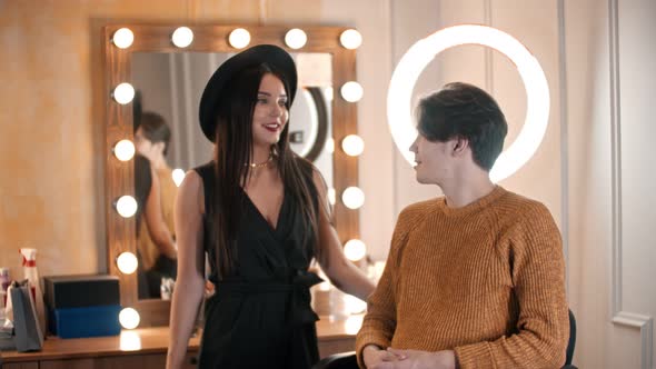 An Attractive Male Model Sitting in the Chair and Woman Make Up Artist About To Apply Makeup on His