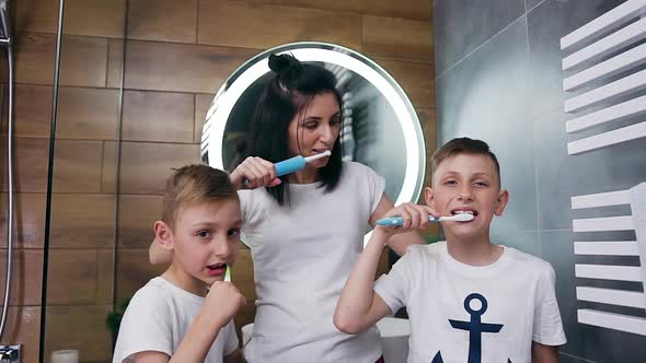 Happy Mother and Her Sons Cleaning Together Their Teeth Using Brushes in the Bathroom