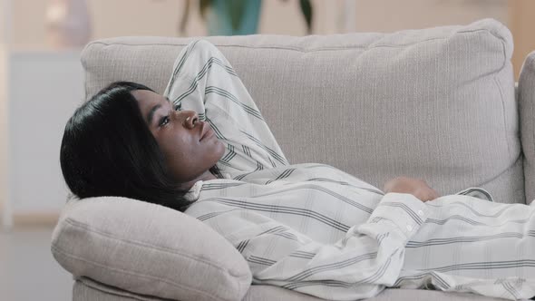 Young Pensive Calm Dreaming African American Woman Resting on Comfortable Sofa in Living Room