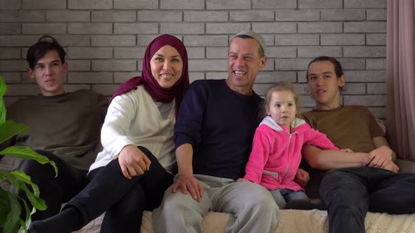 A happy middle eastern Muslim family sits together on the sofa and laughs. Ramadan holiday