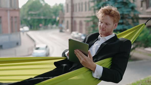 Redhead Business Lying in Hammock and Working on Tablet