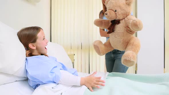 Happy woman giving a teddy bear to a girl in a bed