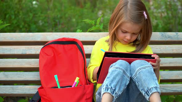 Girl Sits on Bench in Schoolyard and Does Homework