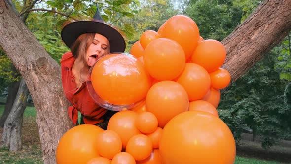 Beautiful girl in an orange shirt, black skirt and witch hat. Licks the balloons. Halloween.
