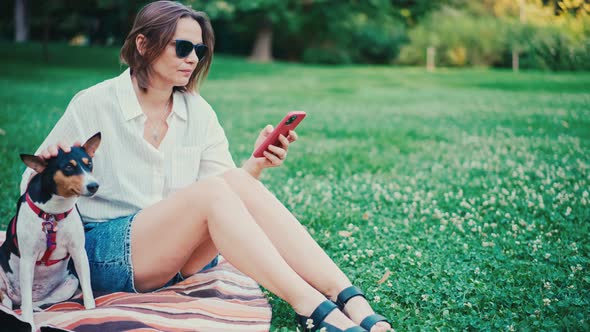 A Young Adult Woman Sits on a Blanket in the Park with Her Basenji Dog