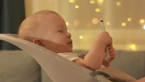 Baby Boy Sits in Rocking Chair and Holds Remote Control From TV Digital Media Player