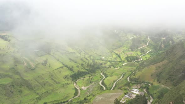 Aerial view flying between the clouds over a  valley with a dirt road curving through farm meadows