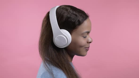 Mixed Race Woman Dancing with Wireless Headphones Isolated on Pink Studio Background