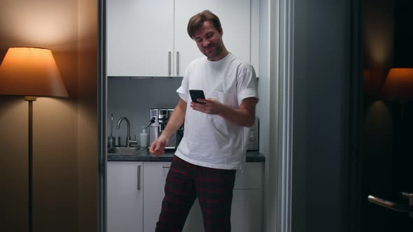 Excited Man in Pajamas Receive Good News on Smartphone and Do Winner Gesture Standing in Kitchen