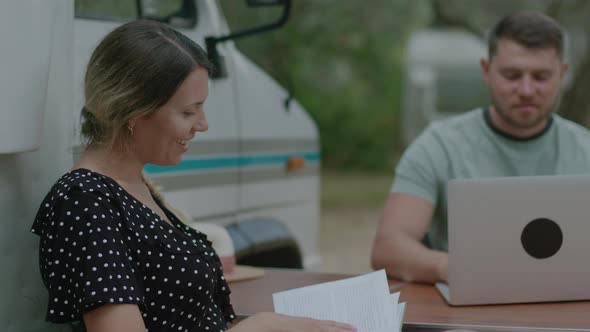 Traveler Man working at laptop and woman reading the book in summer camping.