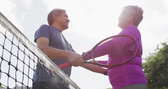 Video of happy biracial senior couple embracing on tennis court
