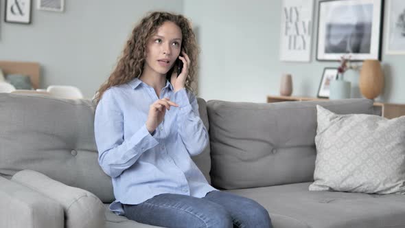 Young Curly Hair Woman Talking on Phone while Relaxing on Sofa