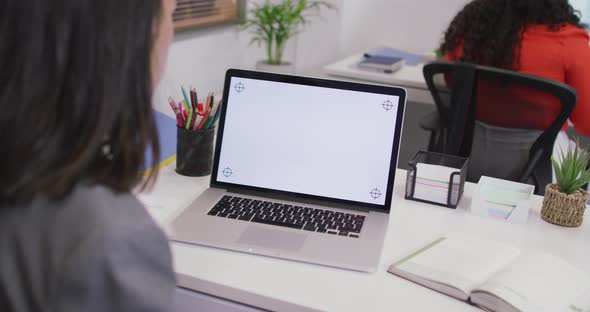 Biracial businesswoman sitting at desk, using laptop with copy space in modern office