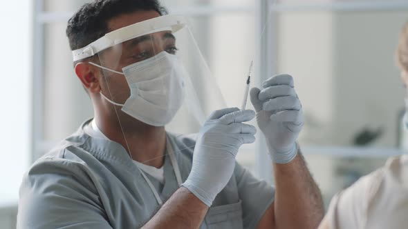 Doctor in Protective Uniform Vaccinating Female Patient