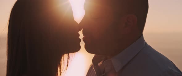 Close up of a young couple kissing at sunset, with beautiful sun flare behind them. 