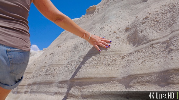 4K Closeup of woman hand touching white sandy texture rock wall formation at Sarakiniko, Greece