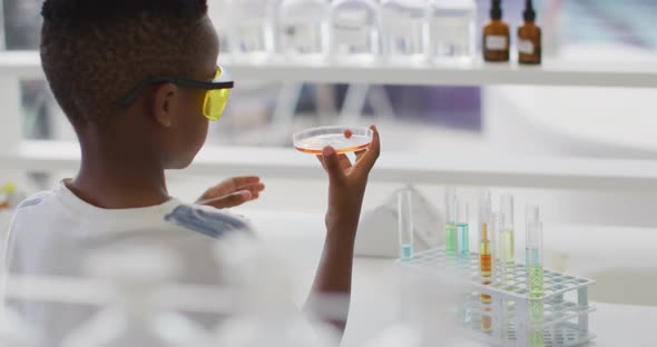 Video of happy african american boy wearing glasses and holding reagent during chemistry lesson