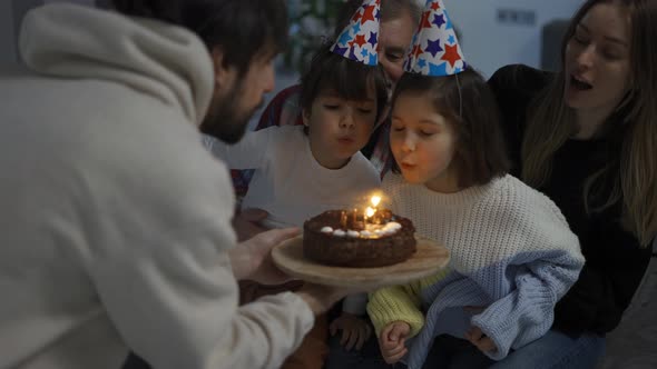 Little Brother and Sister Blows Out the Candles on Cake Together in a Circle of Happy Family