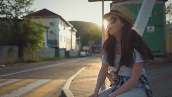 A young woman is sitting outside in the shade, hiding from the setting hot sun.