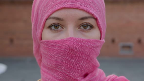 Attractive Muslim Woman with Natural Make Up Wearing Pink Hijab Scarf Looks at Camera