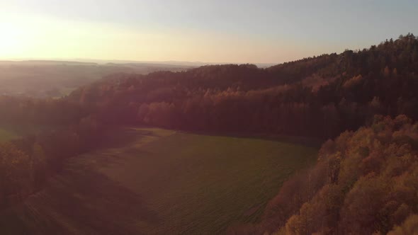 AERIAL: Drone flying above an autumn forest and fields during sunset