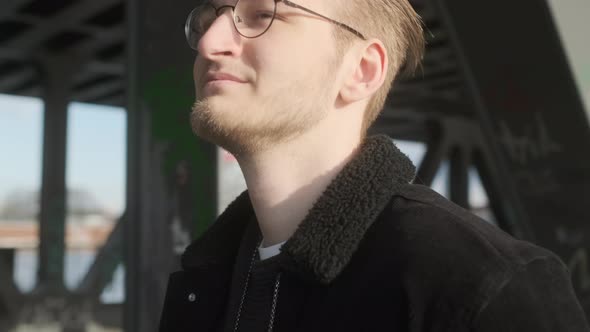 Young European Man with Glasses, Beard and Man Bun Walking on Sidewalk on a Sunny Evening in Hamburg