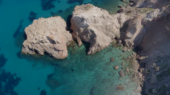 Top Down Aerial Zoom Out of Cliffs Cascading into the Blue Aegean Sea in Milos