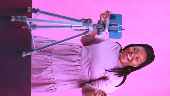 Dark Skinned Woman Laughing and Shooting Social Media Stories in Pink Wall Background